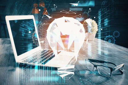 Computer on desktop in office with bulb icon hologram. Multi exposure. Concept of idea.