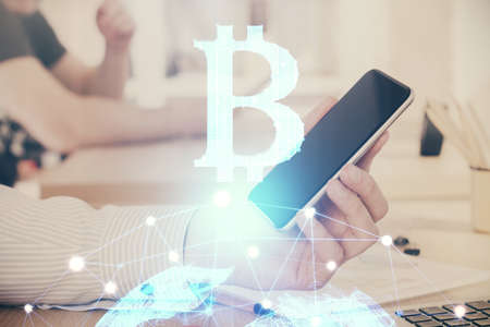 Double exposure of mans hands holding and using a phone and crypto currency blockchain theme...