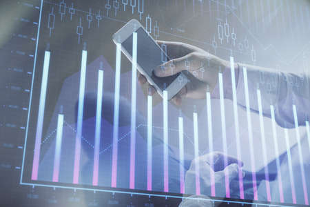 Double exposure of mans hands holding and using a digital device and forex graph drawing. Financial...