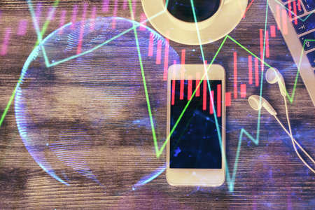 Double exposure of forex chart hologram over desktop with phone. Top view. Mobile trade platform...