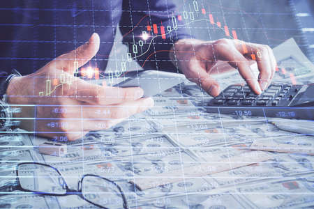 Double exposure of mans hands holding and using a digital device and forex graph drawing. Financial...