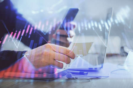 Double exposure of mans hands holding and using a phone and financial graph drawing. Analysis...