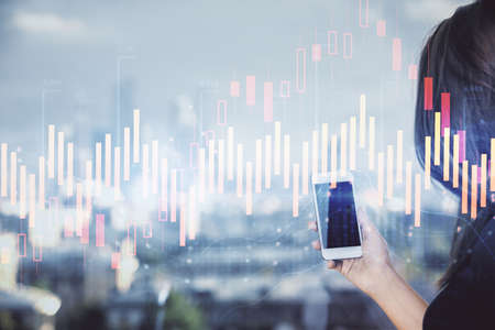 Double exposure of forex chart sketch hologram and woman holding and using a mobile device. Stock market concept.の写真素材