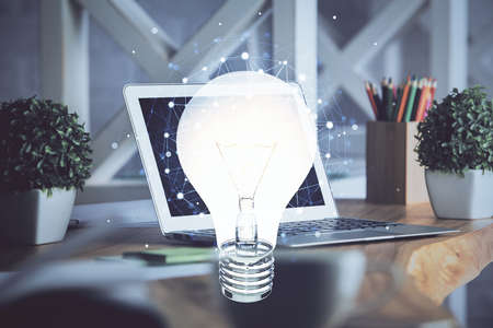 Computer on desktop in office with bulb icon hologram. Double exposure. Concept of idea.の写真素材