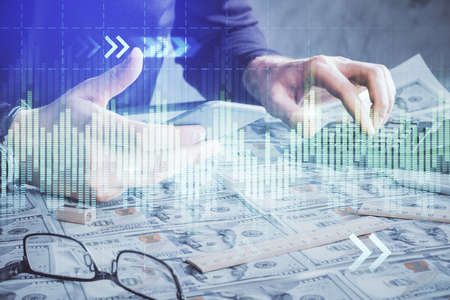 Double exposure of mans hands holding and using a digital device and forex graph drawing. Financial...