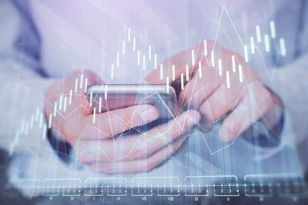 Double exposure of mans hands holding and using a digital device and forex graph drawing. Financial...