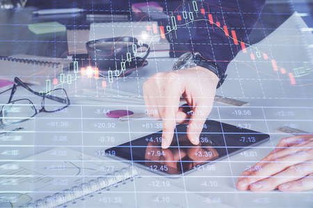 Double exposure of mans hands holding and using a digital device and forex graph drawing. Financial...