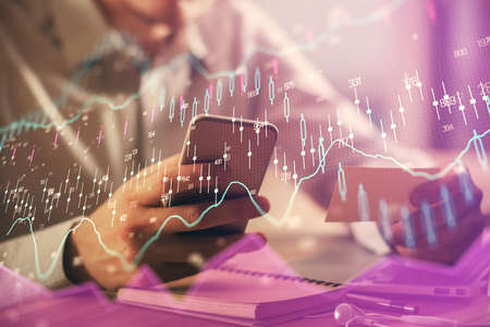 Double exposure of mans hands holding and using a phone and financial graph drawing. Analysis...