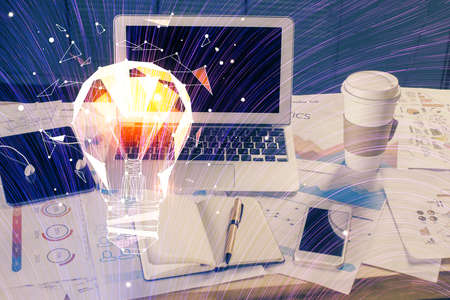 Computer on desktop in office with bulb icon hologram. Multi exposure. Concept of idea.