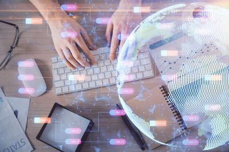 Multi exposure of mans hands typing over computer keyboard and world map hologram drawing. Top view....