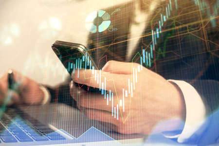 Multi exposure of mans hands holding and using a digital phone and forex graph drawing. Financial...