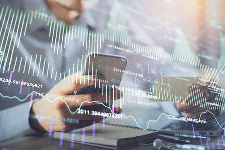 Double exposure of mans hands holding and using a phone and financial graph drawing. Analysis...