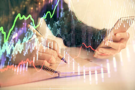 Double exposure of forex graph sketch hologram and woman holding and using a mobile device. Stock...