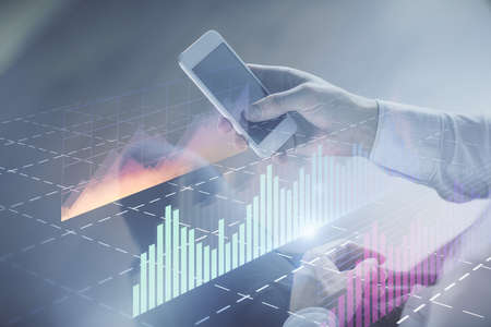 Double exposure of mans hands holding and using a digital device and forex graph drawing. Financial...