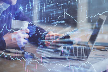 Double exposure of mans hands holding and using a phone and financial graph drawing. Analysis...
