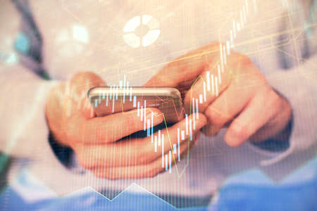 Multi exposure of mans hands holding and using a digital phone and forex graph drawing. Financial...