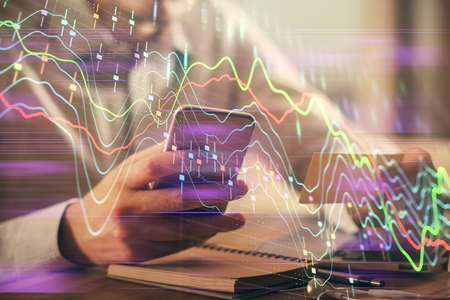 Double exposure of mans hands holding and using a phone and financial graph drawing. Analysis...