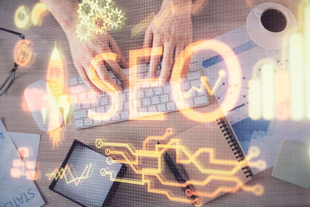 Multi exposure of man's hands typing over computer keyboard and SEO hologram drawing. Top view. Search optimization concept.の写真素材
