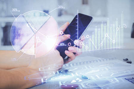 Double exposure of man's hands holding and using a digital device and forex graph drawing. Financial...