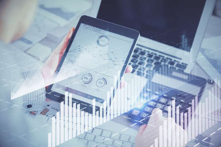 Double exposure of mans hands holding and using a digital device and forex graph drawing. Financial...