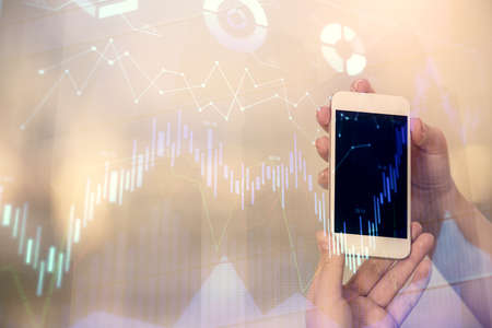 Double exposure of forex chart sketch hologram and woman holding and using a mobile device. Stock...