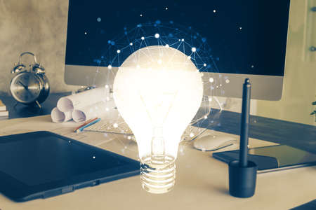 Computer on desktop in office with bulb icon hologram. Multi exposure. Concept of idea.の写真素材