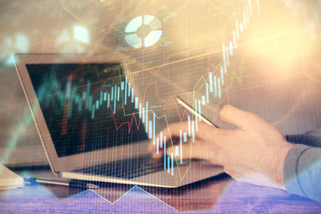Double exposure of mans hands holding and using a digital device and forex graph drawing. Financial...