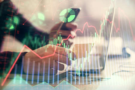 Double exposure of mans hands holding and using a phone and financial graph drawing. Analysis...