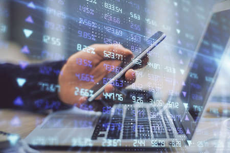Double exposure of mans hands holding and using a phone and financial graph drawing. Analysis...