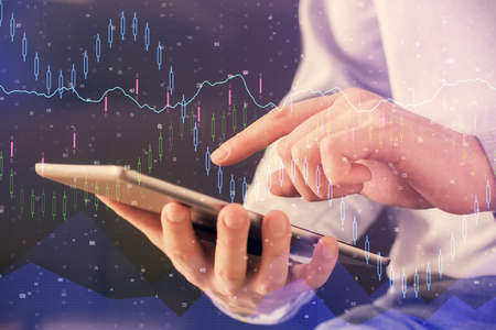 Double exposure of mans hands holding and using a digital device and forex graph drawing. Financial...