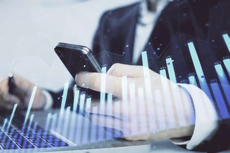 Multi exposure of mans hands holding and using a digital phone and forex graph drawing. Financial...