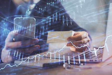 Double exposure of mans hands holding and using a phone and financial graph drawing. Analysis concept.の写真素材