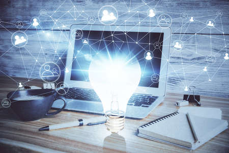 Computer on desktop in office with bulb icon hologram. Double exposure. Concept of idea.の写真素材