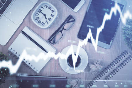 Double exposure of financial chart hologram over desktop with phone. Top view. Mobile trade platform...