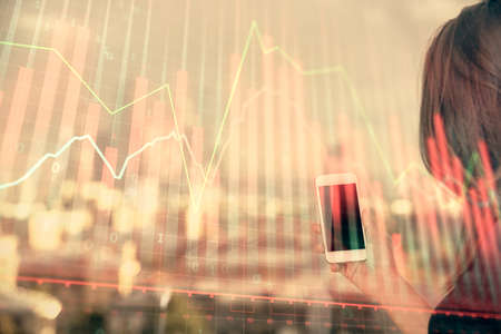 Double exposure of forex chart sketch hologram and woman holding and using a mobile device. Stock market concept.の写真素材