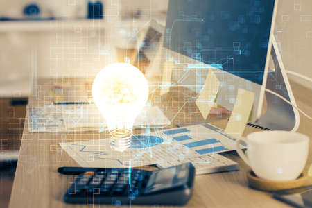 Computer on desktop in office with bulb icon hologram. Multi exposure. Concept of idea.の写真素材