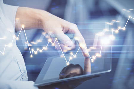 Double exposure of mans hands holding and using a digital device and forex graph drawing. Financial...