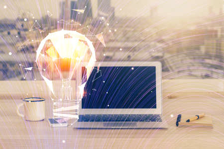 Computer on desktop in office with bulb icon hologram. Multi exposure. Concept of idea.