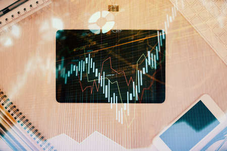 Double exposure of forex graph hologram over desktop with phone. Top view. Mobile trade platform...