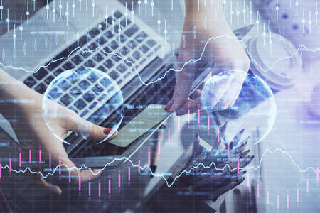 Double exposure of businesswoman hands typing on computer and financial graph hologram drawing....