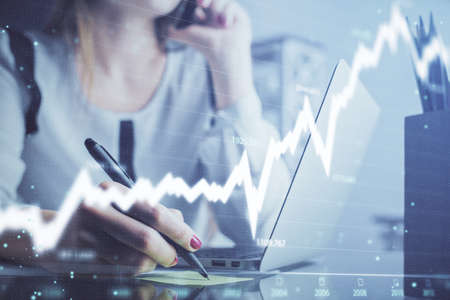 Double exposure of woman hands typing on computer and financial graph hologram drawing. Stock market...