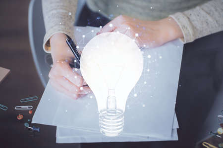 Bulb hologram over hands taking notes background. Concept of idea. Double exposureの写真素材