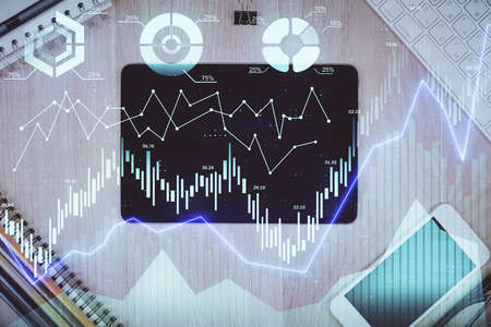Double exposure of forex graph hologram over desktop with phone. Top view. Mobile trade platform...