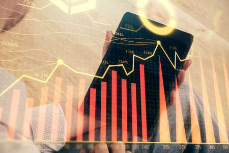 Double exposure of mans hands holding and using a digital device and forex graph drawing. Financial...