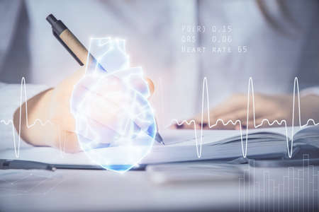 Heart hologram over womans hands writing background. Concept of Medical education study. Double exposureの写真素材