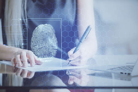 Blue fingerprint hologram over womans hands taking notes background. Concept of protection. Double exposureの写真素材