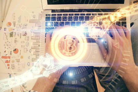 Double exposure of mans hands typing over computer keyboard and crypto currency theme hologram...