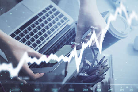 Double exposure of businesswoman hands typing on computer and financial graph hologram drawing....