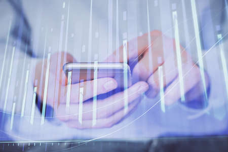 Double exposure of mans hands holding and using a digital device and forex graph drawing. Financial...