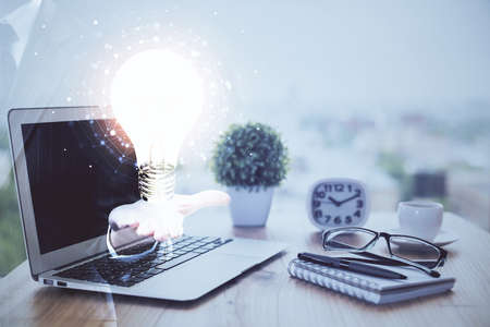 Computer on desktop in office with bulb icon hologram. Double exposure. Concept of idea.の写真素材